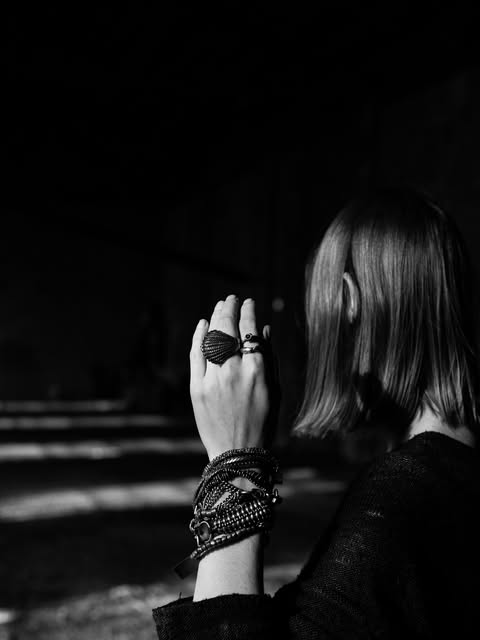 A raised hand wearing a shell ring and stacked chain bracelets — black-and-white photograph