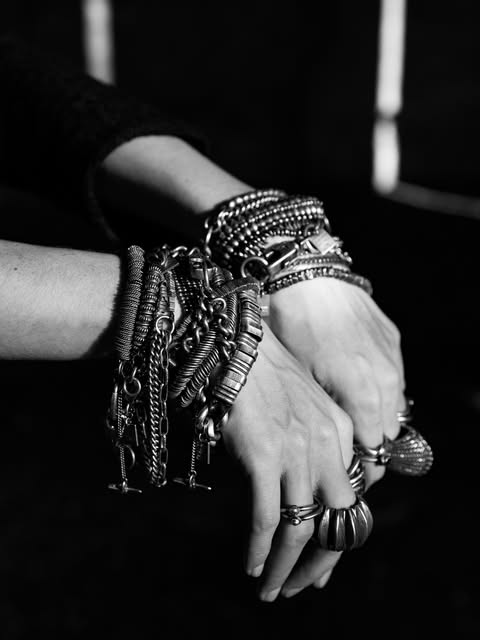 Crossed hands wearing stacked oxidised-silver bracelets and rings — black-and-white photograph